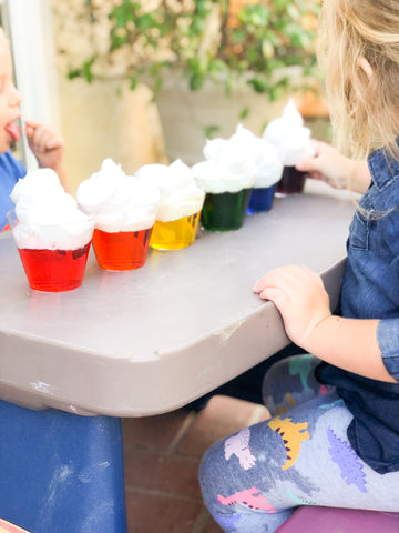 clear cups filled with rainbow colored water and topped with shaving cream for sensory play