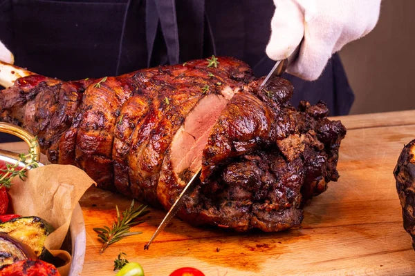 Juicy Roasted Leg of Lamb Being Carved Chef slicing a roasted leg of lamb on a wooden cutting board..