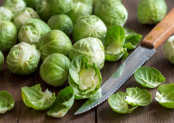 Fresh Brussels sprouts on a wooden surface with a serrated knife and loose leaves