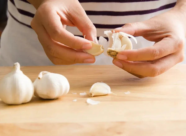 Person peeling fresh garlic cloves on a wooden cutting board