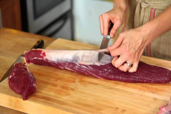Person trimming silver skin off beef tenderloin on a cutting board