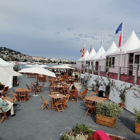 L'espace festival de Cannes orné de drapeaux français, de tables et de parasols blancs.