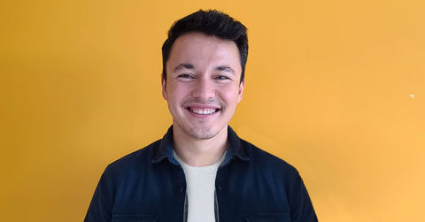 Un homme souriant face à la caméra sur fond jaune.