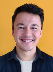 A smiling man facing the camera against a yellow background.