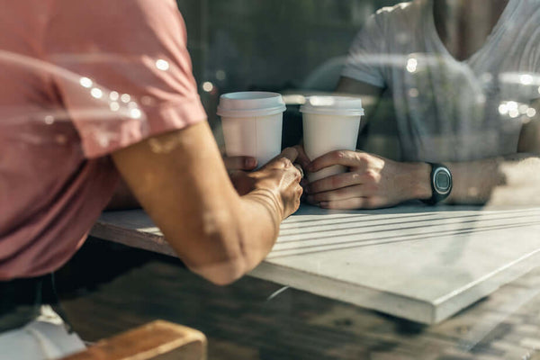 Two people sit at a table inside a coffee shop, coffee in hand