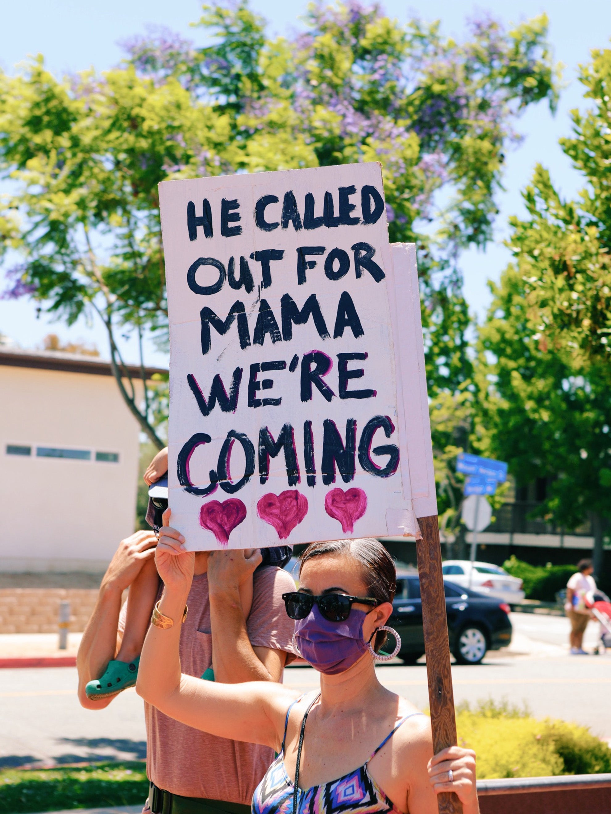 Woman holding a sign that says, "HE CALLED OUT FOR HIS MAMA WE'RE COMING"