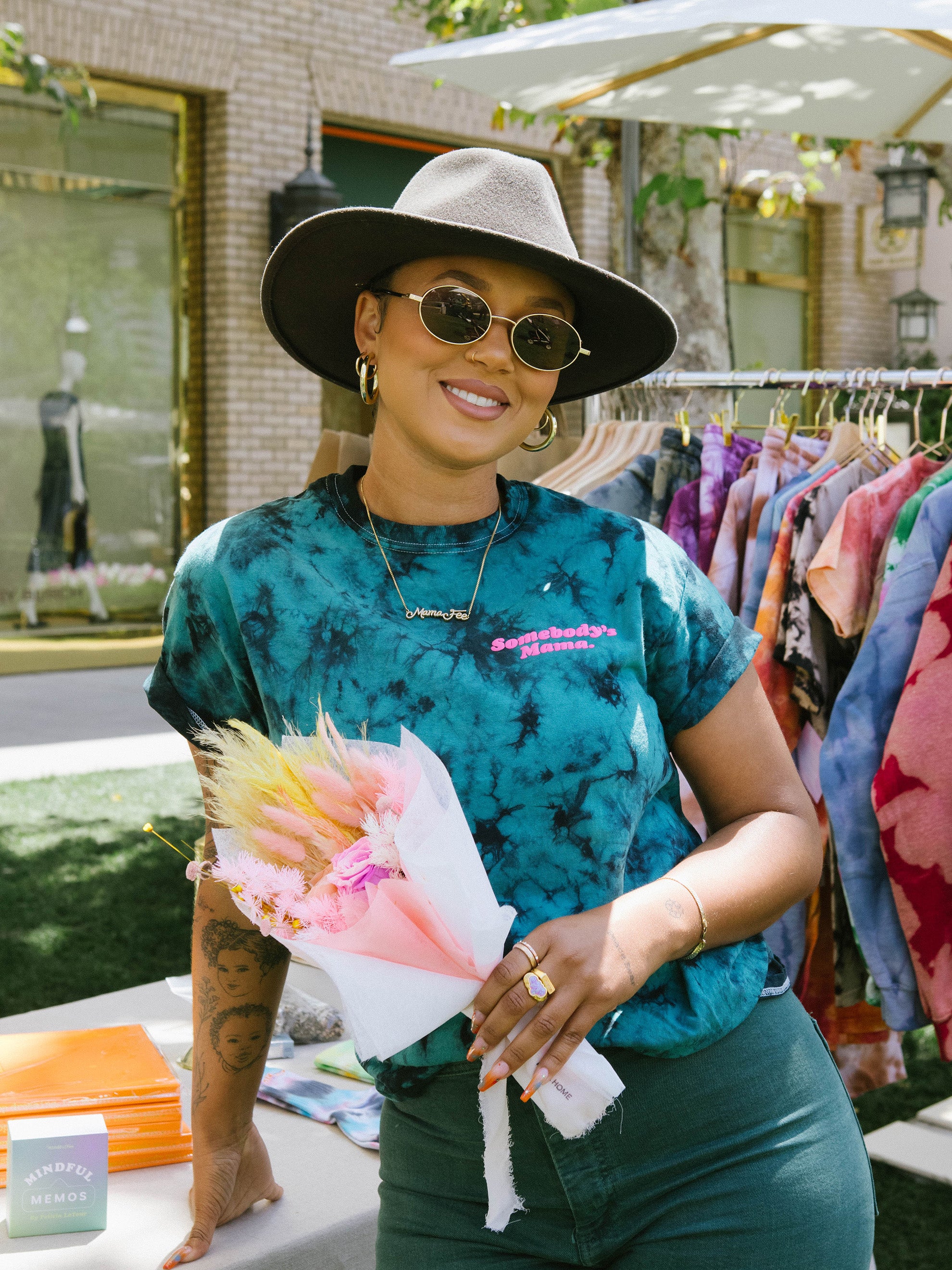 Felicia wearing a teal and black MindfulFee shirt while holding a small pink bouquet of flowers in her hand