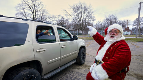 Santa waving to a kid in a large SUV who is also waving back