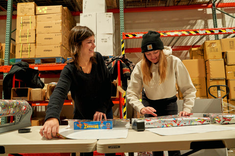 Two girls wrapping Christmas presents with a warehouse in the background