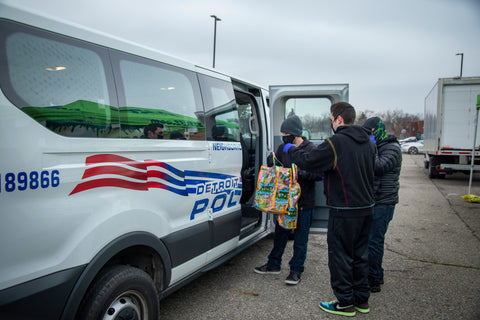 Team members of the Ooze Foundation load bags of side dishes off a Detroit police van to be put into people's trunks.
