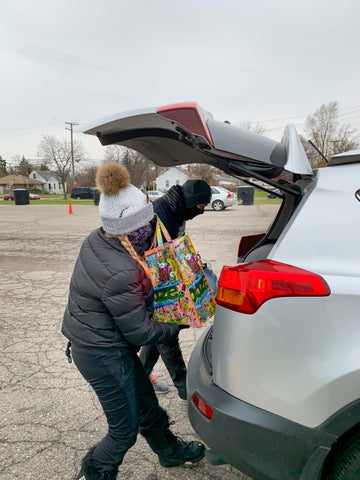 Ooze Foundation team members load a Thanksgiving dinner into a car trunk. They are wearing winter clothes and masks, and have a turkey and bag of side dishes in hand.