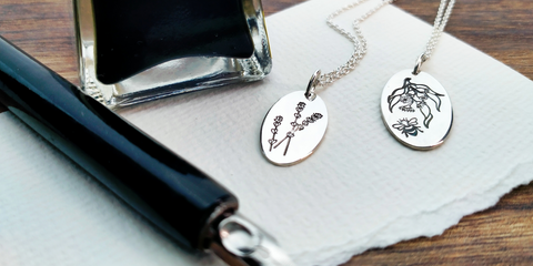 Oval Lavender and Gumnut Bee Pendants by Darling Bee set beside an ink bottle and pen