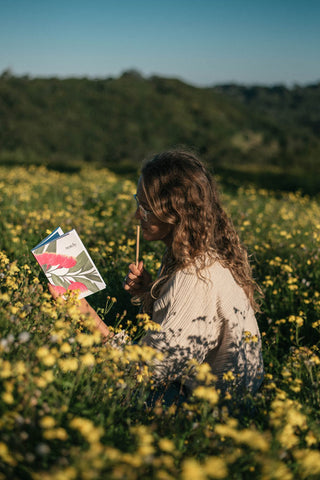 Journaling in Notely Blossom Journal in field of yellow wild flowers 