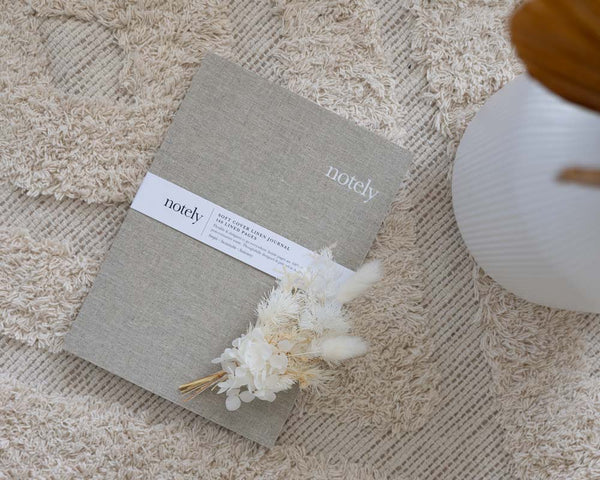 Linen Notely journal on white rug with flowers on top