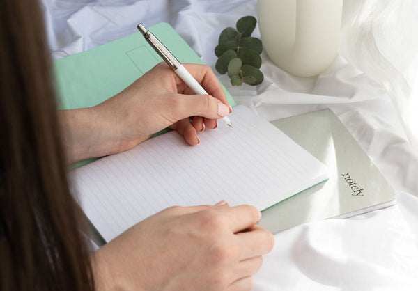 Woman writing goals in a Notely notebook with minty green cover