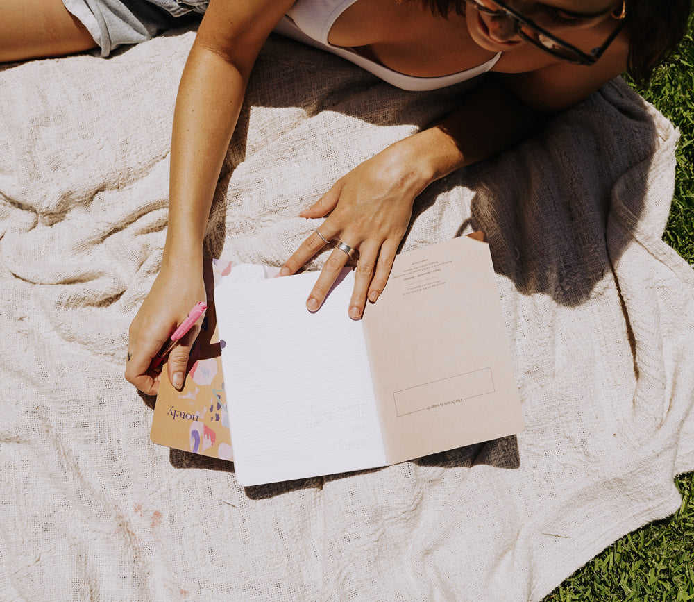 Journaling in Notely notebook on a picnic rug