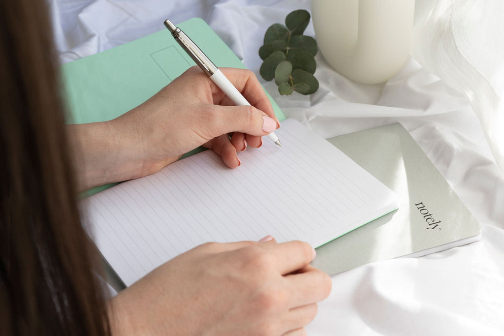 Writing in a Notely Notebook with minty green cover and a white pen