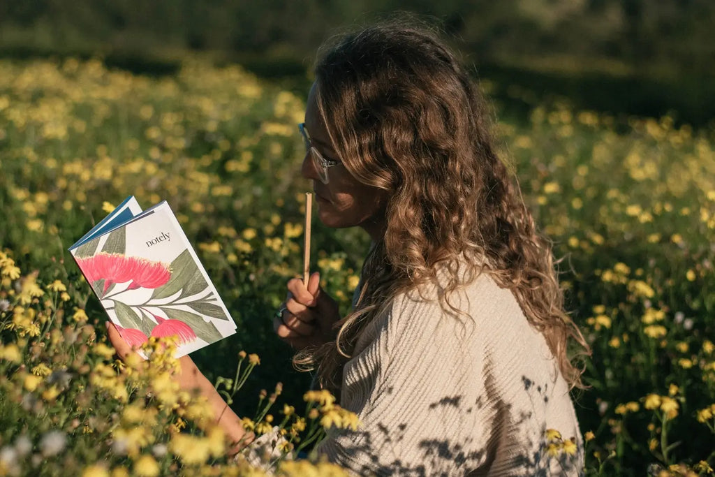 Woman journaling in a flower field with Blossom notebook