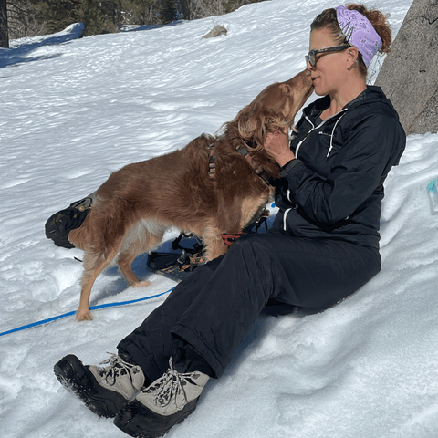 A dog licks Cory's face while they sit in the snow