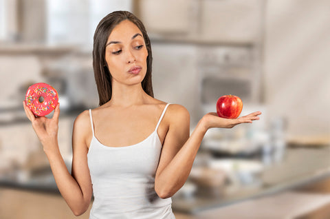 Woman holding a donut in one hand and an apple in the other.