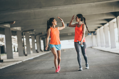 Two women hi fiving and walking outdoors.