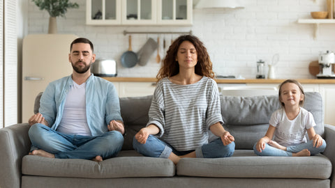 Couple and little daughter sitting on couch meditating on couch.