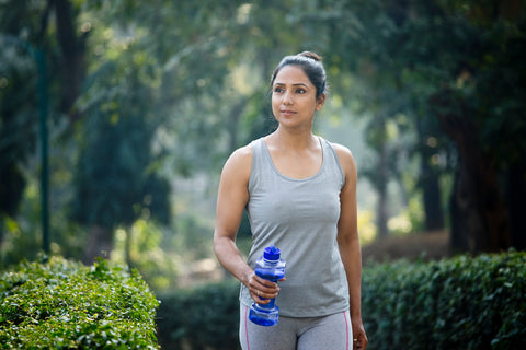 Woman wearing walking clothes and a bottle of water walks outside.