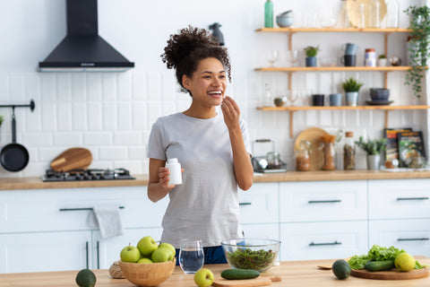 Women standing in kitchen eating salad. Green vegetables sit in bowls on the counter she stands in front of.