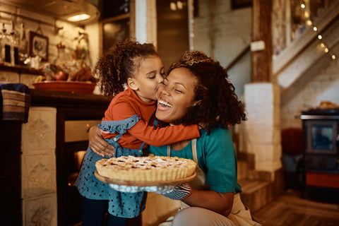 Smiling woman hugging child while holding a pie in her left hand.