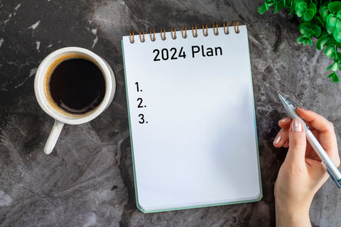 2024 plan book with a coffee on the left and a person holding a pen on the right..