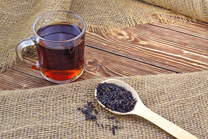 Cup of black tea on the table with a spoon of dried leaf tea