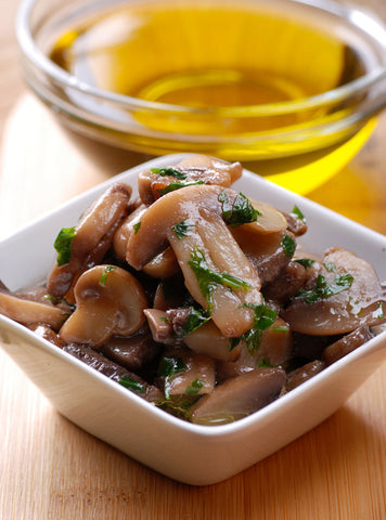 bowl of cooked mushrooms with a bowl of oil in the background