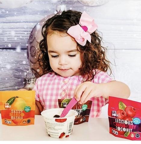 Three year old girl eating her It's Nola Snacks with yogurt. 