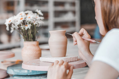 woman painting clay vase in pottery class