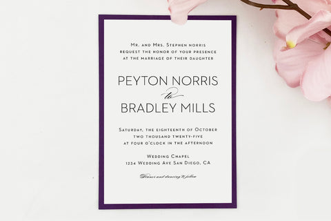 A white wedding invitation mounted on purple cardstock backing on a white background with flowers.