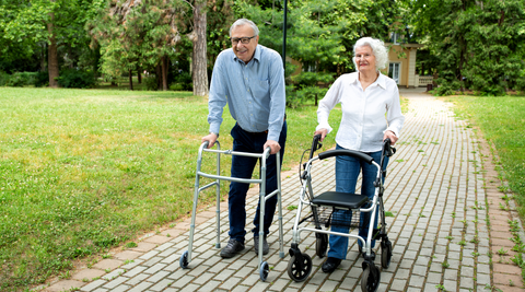 A happy couple walking in the park using mobility aids.