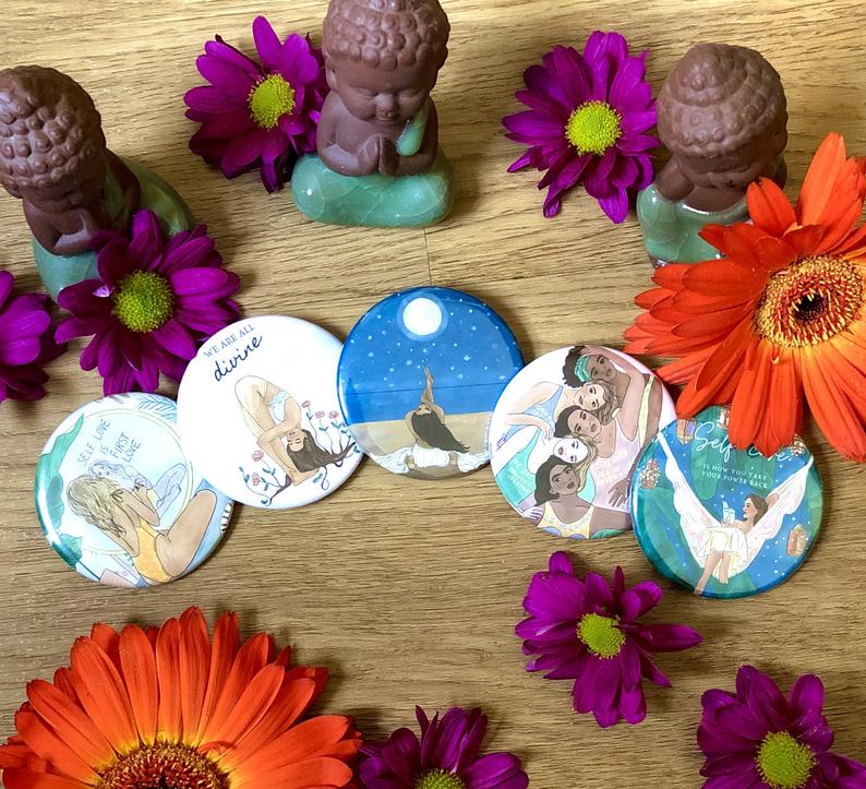 Noharanda pin badge designs, displayed on a desktop with flowers