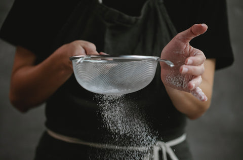 A person sprinkling flour with a sieve