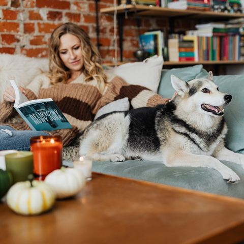 Women sitting on couch reading book with her dog