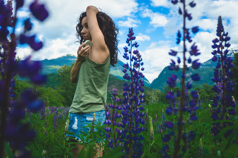 women using natural deodorant bar in field of purple lupine flowers