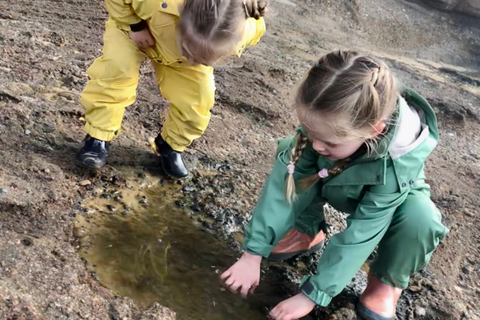 two young girls in waterproof nature play clothes exploring rockpools
