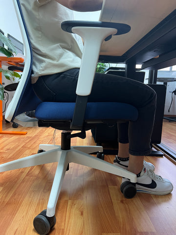 Persona sentada en una silla de oficina, con los pies sobre el piso y sus rodillas a 90 grados.