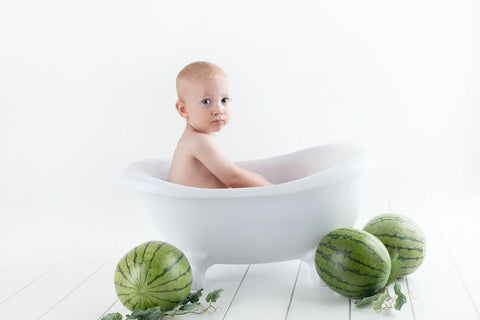 a baby in a bathtub with watermelons for wheels