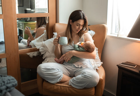 a mother holding their baby and a cup of sea while sat on a chair