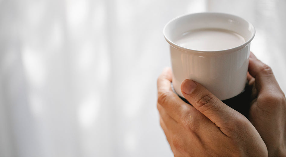 A close-up on a pair of hands holding a cup of tea with warm milk.