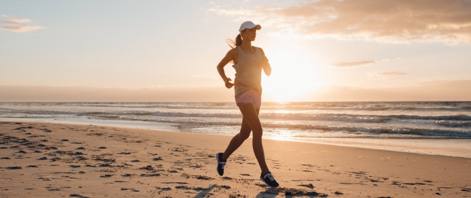 A woman is running on a beach with the sun setting behind her.