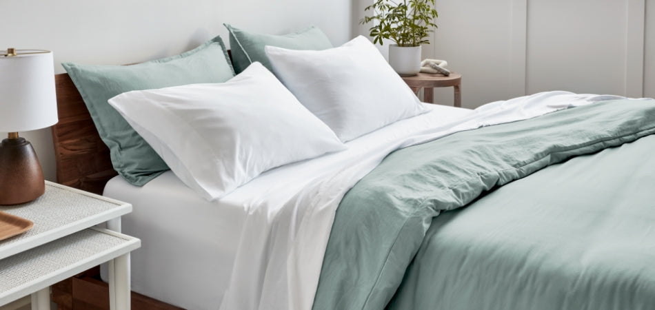 A bed made with white sheets and a sandwashed duvet cover. The duvet cover is folded back over itself part way down the bed and the top sheet is folded over the duvet cover.