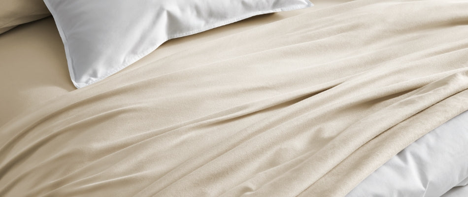 Close up of a top sheet folded back over a white comforter on a bed. The edge of a white pillowcase is visible. 