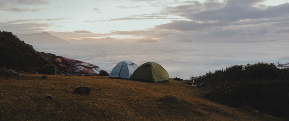 Two tents are pitched next to each other overlooking the sea.  It is sunrise and the air is misty.