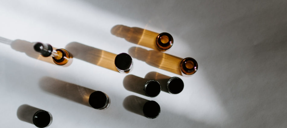 Small glass bottles on a white surface with sun shining on them creating shadows.